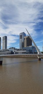 Modern buildings by river against sky in city