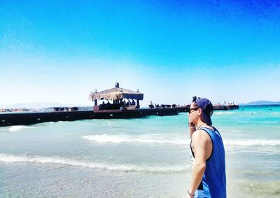 Side view of man walking at beach by pier against sky