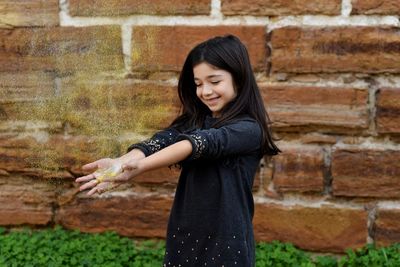Smiling young woman standing against brick wall