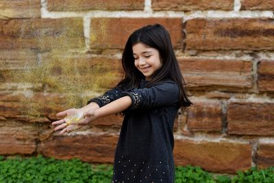 Playful girl playing with glitter against brick wall