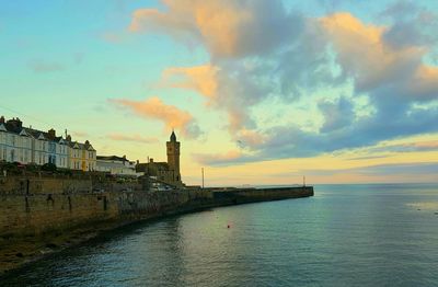Scenic view of sea by buildings against sky during sunset