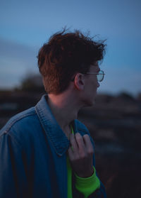 Close-up of young man looking away against sky during sunset