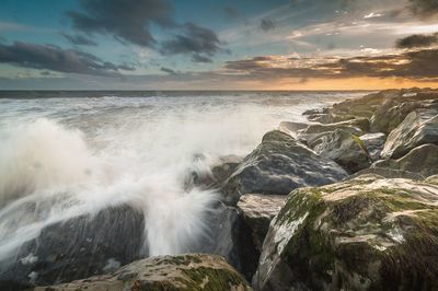 Waves splashing on rocks in sea during sunset