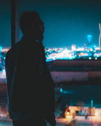 Side view of man looking at illuminated city at night