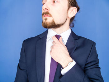 Young businessman adjusting tie against blue background