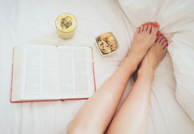 Low section of woman reading book on bed