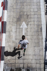 From above young guy with leg prosthesis running up paved slope against shabby building during workout on city street