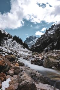 Scenic view of stream amidst rocks against sky during winter