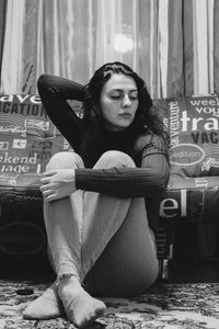 Young woman with hand in hair sitting on floor at home