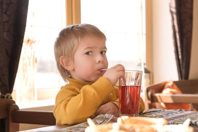 Child boy baby drinking lemonade in cafe. 3 years kid drinks red juice from glasses through straws.