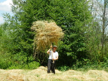 Portrait of man holding hay with stick while standing against trees