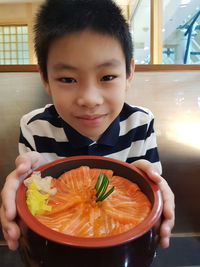 Portrait of boy holding food while sitting in restaurant