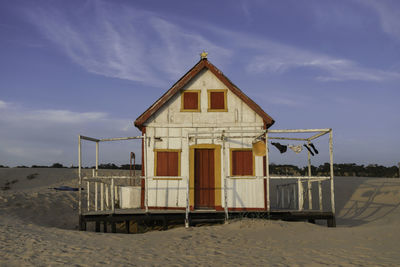 Hut on beach by house against sky