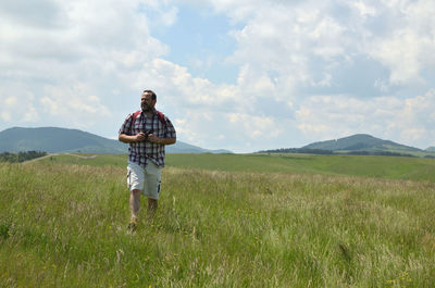 Man with a backpack and binoculars hiking through mountain meadow on a spring day.