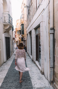 Rear view of woman walking on footpath amidst buildings