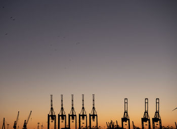 Silhouette cranes against clear sky during sunset