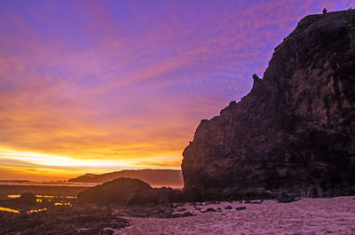 Rock formation by sea against sky during sunset