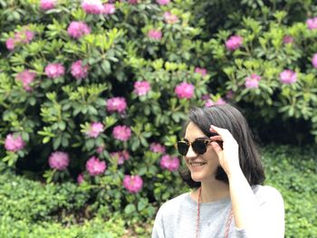 Smiling young woman standing against pink flowering plants