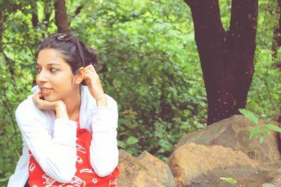 Young woman holding camera against trees