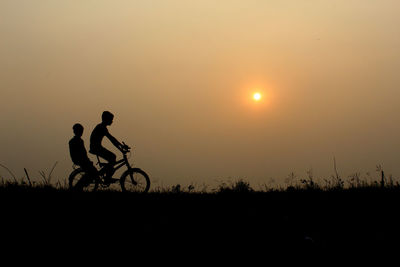 Silhouette boys on bicycle against sky during sunset