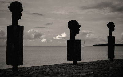 Silhouette sculpture on wooden post by sea against sky