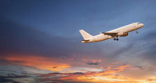 Low angle view of airplane flying against sky during sunset