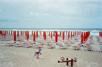 Hooded chairs on beach against sky