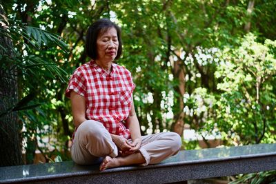 Woman sitting on bench against trees