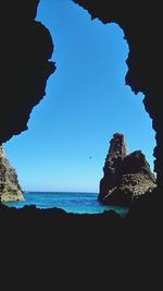 Silhouette rock formations by sea against clear blue sky