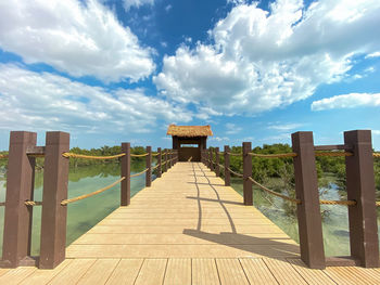 View of wooden footbridge against cloudy sky