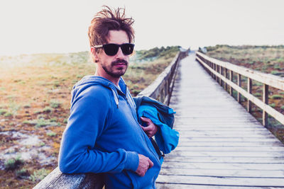 Portrait of young man wearing sunglasses standing against railing