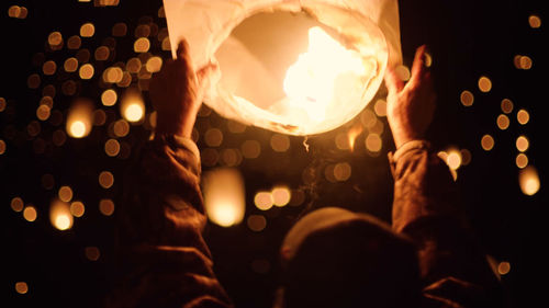 Cropped image of man holding lit paper lantern at night