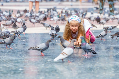 A beautiful caucasian girl, 6-7 years old, feeding pigeons at plaza de catalunya in barcelona. 