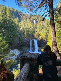 Rear view of woman standing by waterfall in forest