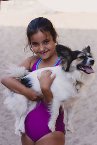 Portrait of smiling girl in swimwear holding dog at beach