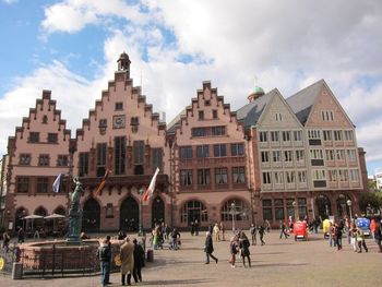 People walking in city against cloudy sky