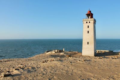 Lighthouse on beach against clear blue sky