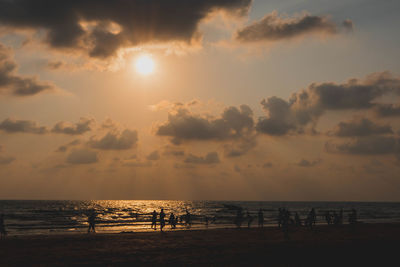 Silhouette people on beach against sky during sunset