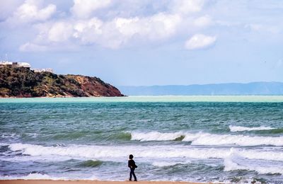 Silhouette boy walking on calm beach