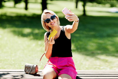 A blonde girl is sitting on a park bench and eating hot corn, resting after a walk, taking photos