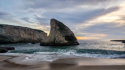 Rock formation on beach against sky during sunset