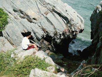 High angle view of man sitting on rocks by sea