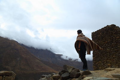 Rear view of man standing on rock against sky