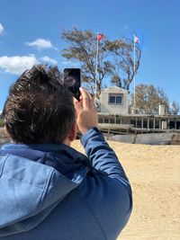 Rear view of man photographing against sky