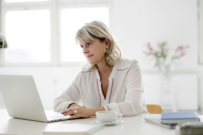 Smiling mature businesswoman working on laptop at desk