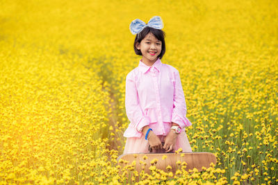 Portrait of smiling girl with case standing amidst yellow flowers on field