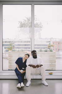 Full length of tired female nurse leaning on male doctor's shoulder against window at hospital