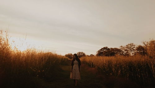 Woman standing amidst plants on field against cloudy sky