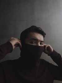 Portrait of young man holding covering face against wall