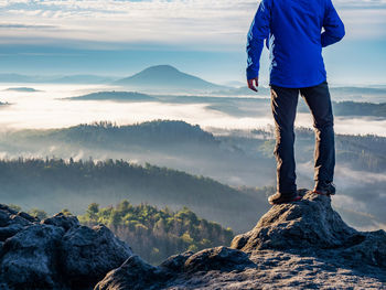 Man watch thick mist in valley from rocky view point in mountains. hiker climbed up alone 